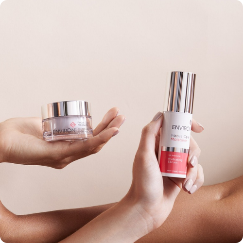 Twee flacons van de Environ Focus Care Moisture+ lijn, de Vita-Complex Super Moisturiser en het Intense Alpha Hydroxy Gel, liggend op een spiegelende ondergrond.