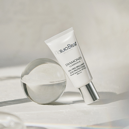 De tube Diamond Luminous zonnebrandcrème rust tegen een glazen bol in een heldere, minimalistische setting.