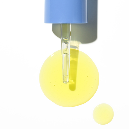 Close-up van een blauwe pipet die geelkleurig serum laat druppelen op een witte achtergrond voor de HydroPeptide Micro Dose Glow Booster.