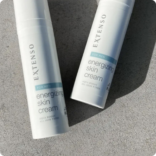 Twee flacons van de Extenso For Men energizing skin cream liggen diagonaal naast elkaar op een lichtgrijze, stenen ondergrond in de zon