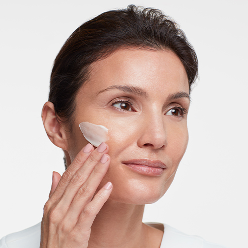 Een vrouw brengende HydroPeptide Power Lift crème aan op haar wang voor huidverzorging.