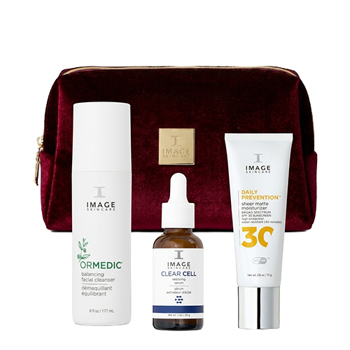 Een bordeauxrode velvet cosmeticatas van IMAGE Skincare met daarvoor drie huidverzorgingsproducten waaronder een reiniger, een serum en een tube dagverzorging.