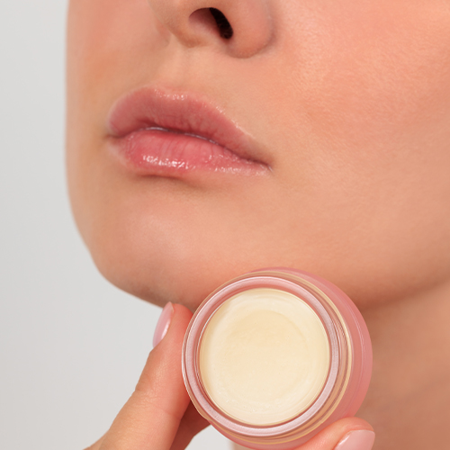 Gezicht van een model met gehydrateerde lippen en een potje lippenbalsem