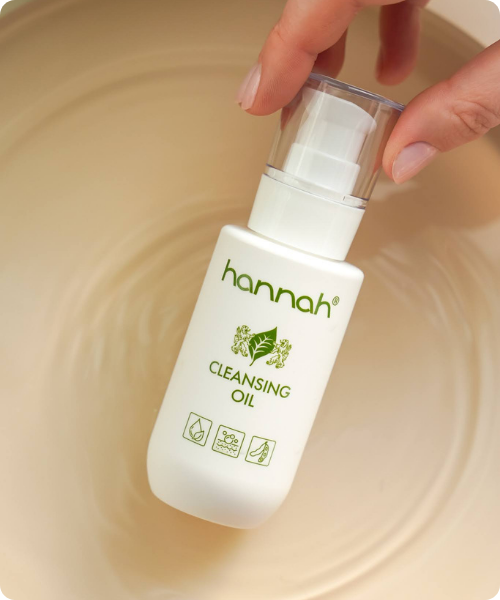 Een witte flacon van hannah Cleansing Oil met een handig pompje, gefotografeerd op een zachte, grijze ondergrond van imitatiebont.