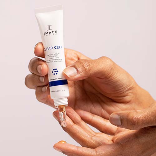 Een hand die de Clear Cell Blemish Gel tube vasthoudt en een druppel gel op een vingertop aanbrengt