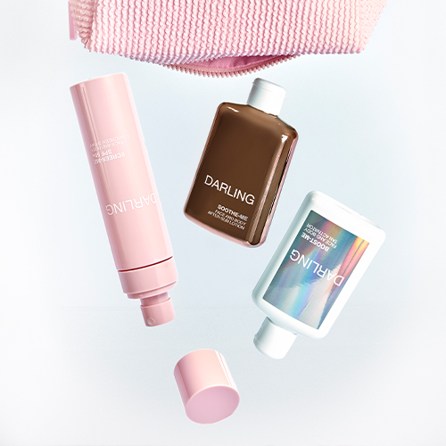 Een creatieve productfoto op een witte achtergrond waar de roze sprayfles, de koperkleurige aftersunfles, de holografische tan activatorfles en de dop van de sprayfles lijken te zweven onder de roze wafel geweven toilettas.