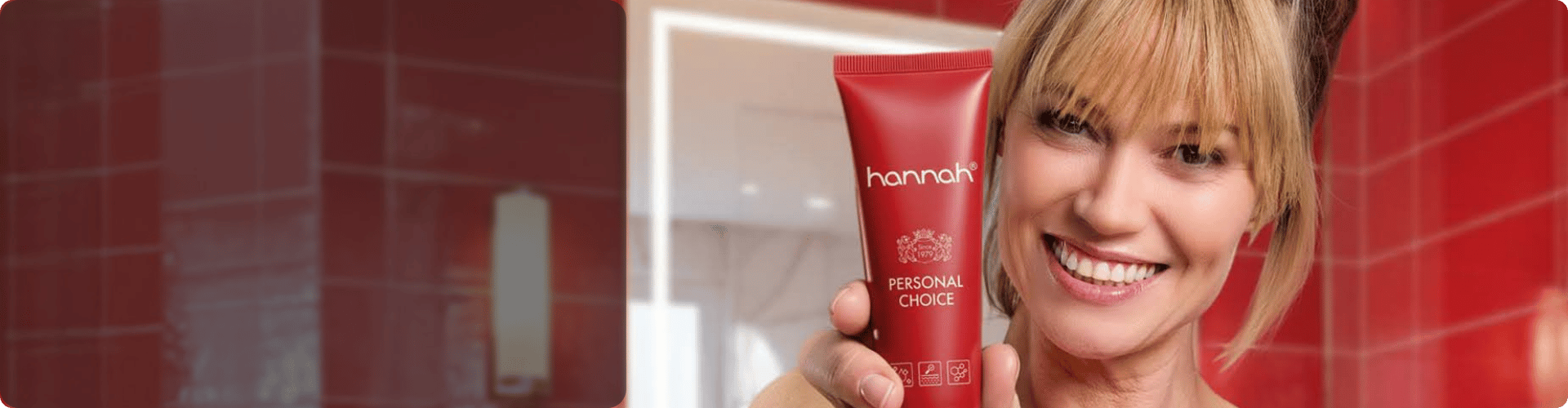 Lachende vrouw die een rode tube hannah Personal Choice vasthoudt in een badkamer met rode tegels
