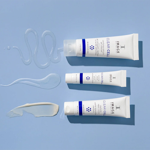Bovenaanzicht van drie IMAGE Skincare tubes met daarnaast de bijbehorende texturen: een transparante gel cleanser, een licht serum en een witte repair crème op een blauwe ondergrond.