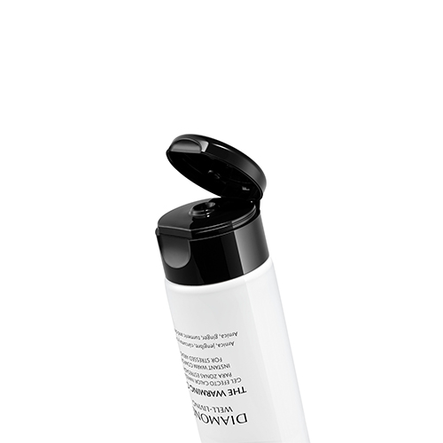 Een close-up van de bovenkant van een witte tube Natura Bisse Diamond Well Living The Warming Gel met een geopende zwarte klikdop tegen een witte achtergrond.
