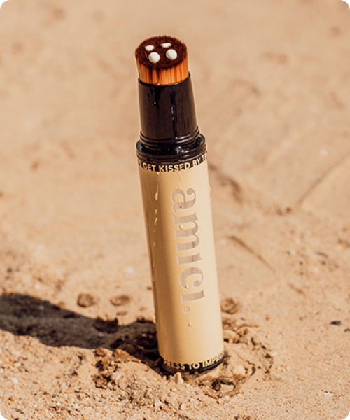 Close up van een Amici hervulbare kwast met SPF creme op de borstelharen staand in fijn beige zand op een zonnige dag