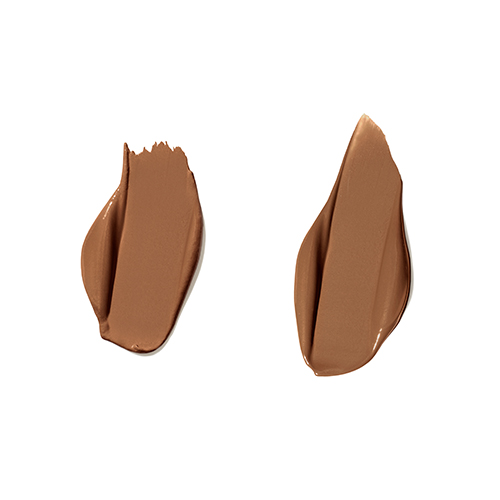 Twee romige vegen van Jane Iredale PureMatch Liquid Concealer in de kleur 12W Dark op een witte achtergrond. De vloeibare textuur toont een donkere, warme tint met een egale dekking