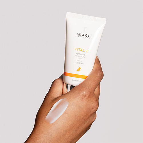 Een hand die de tube VITAL C hydrating water burst vasthoudt met een swatch van het product op de rug van de hand.