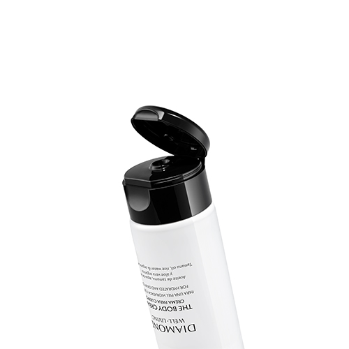 Een schuine close-up van de zwarte klikdop van de Natura Bissé The Body Cream tube, die open staat om de opening en het witte product binnenin te onthullen. De tube is wit met zwarte tekst. De achtergrond is zuiver wit.
