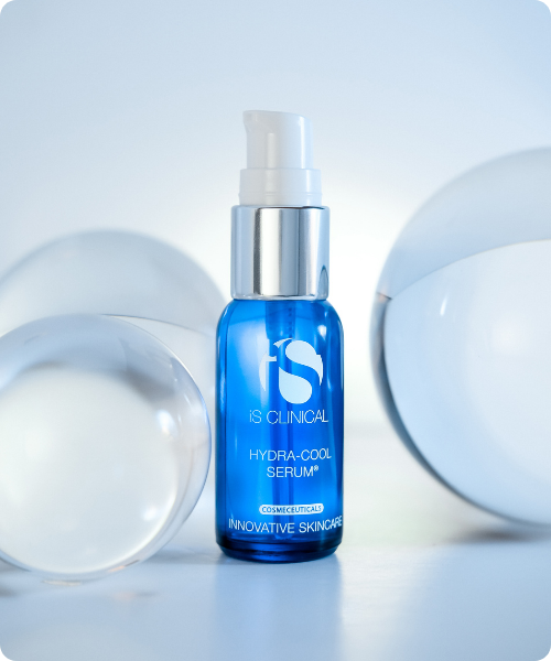 Een blauw glazen flesje iS Clinical Hydra Cool Serum omringd door glazen bollen