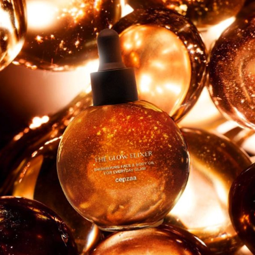 De ronde flacon van Cenzaa The Glow Elixir omringd door dromerige, warme gouden bollen en lichtreflecties die de luxueuze glans van het product benadrukken.