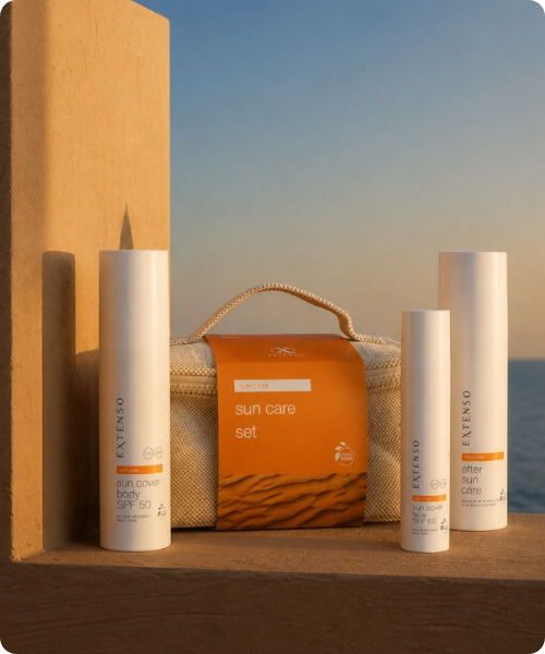 Een Extenso Sun Care set bestaande uit een toilettas en drie flessen zonbeschermingsproducten die op een muurtje voor de zee staan in het warme licht van de ondergaande zon.