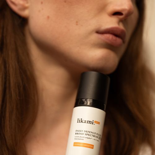 Detailopname van een model dat de Likami Correct + Brighten flacon onder haar kin houdt, met de focus op de verpakking en de huidstructuur.