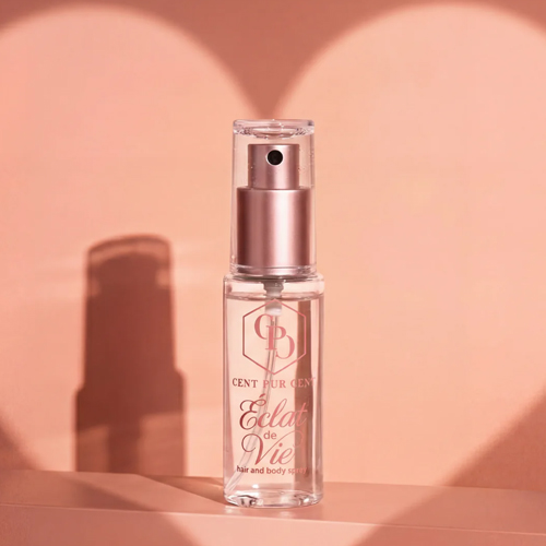 Een flesje Cent Pur Cent Eclat de Vie haar en bodyspray geplaatst op een ondergrond, met op de achtergrond een zachte hartvormige schaduw voor een romantische uitstraling.