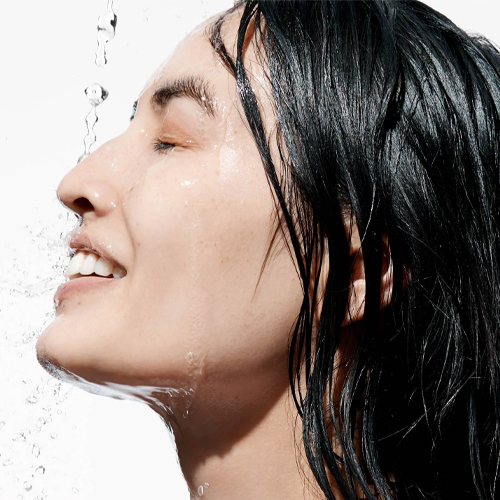 Zijaanzicht van een vrouw die haar gezicht afspoelt met een waterstraal tijdens de huidverzorging