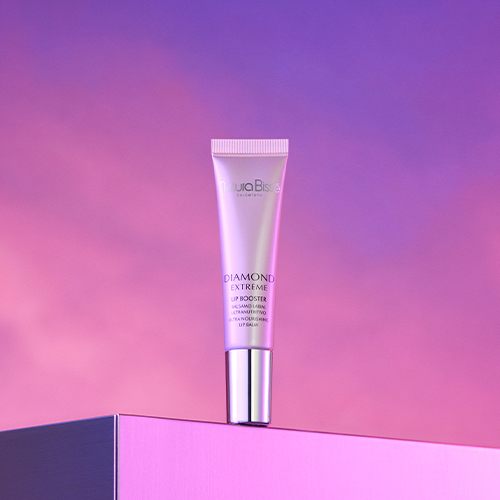 De Natura Bissé Diamond Extreme Lip Booster tube liggend op een minimalistisch stenen plateau naast een helder bergkristal.