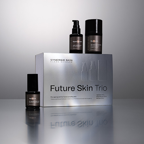Sfeerfoto van de Synergie Skin Future Skin Trio set met de zilveren doos centraal, geflankeerd door de drie bijbehorende huidverzorgingsproducten op een reflecterend oppervlak.