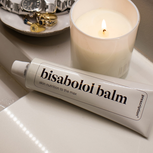 Tube prescription bisabolol balm naast een brandende kaars en een schaaltje met sieraden