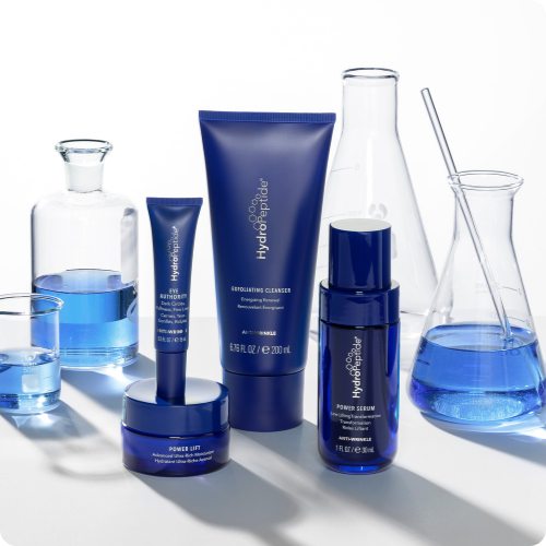 Een verzameling van blauwe HydroPeptide Anti-Wrinkle huidverzorgingsproducten opgesteld op een heldere ondergrond, omringd door laboratoriumglaswerk gevuld met blauwe vloeistof.