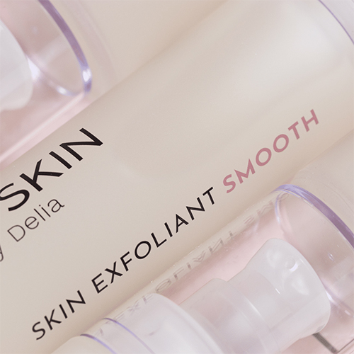 Een close-up shot van meerdere D-SKIN Skin Exfoliant Smooth flacons die netjes naast elkaar liggen in een zachte, roze setting.
