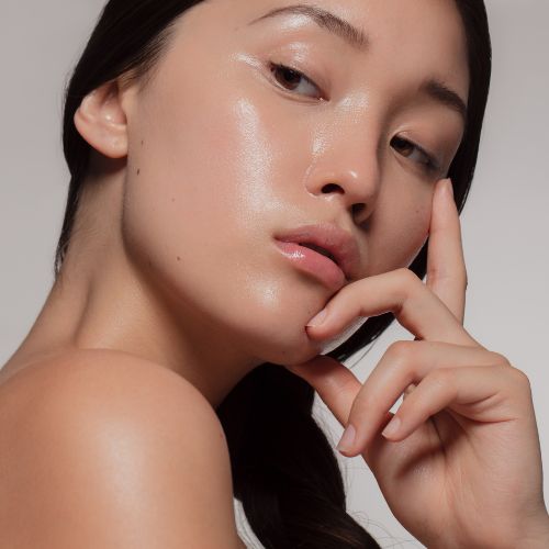 Model met een gezonde, glanzende en gehydrateerde huid die haar gezicht aanraakt