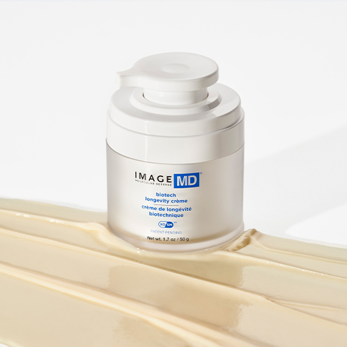 De geopende pot van de IMAGE Skincare MD Biotech Longevity Crème geplaatst op dikke, uitgesmeerde banen van de crème zelf.