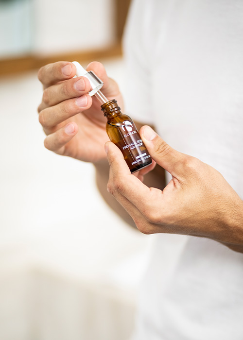 Persoon die een flesje iS CLINICAL Pro-Heal Serum Advance vasthoudt en de druppelaar opent.