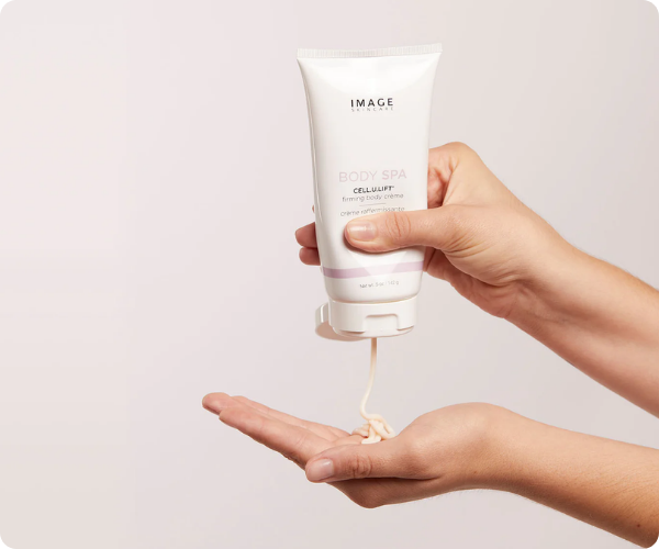Close-up van de IMAGE Skincare Body Spa Cell.U.Lift firming body crème tube die een dikke, rijke crème doseert op een hand.