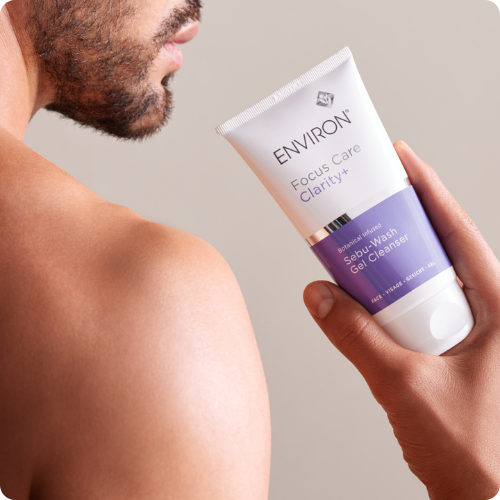 Een hand houdt de tube Environ Focus Care Clarity+ Sebu-Wash Gel Cleanser vast naast de schouder van een man.