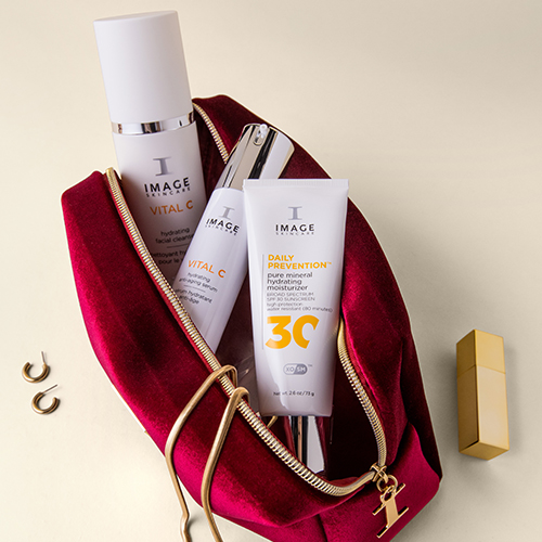 Een open bordeauxrode velvet cosmeticatas van IMAGE Skincare gevuld met diverse huidverzorgingsproducten en gouden accenten op de achtergrond.