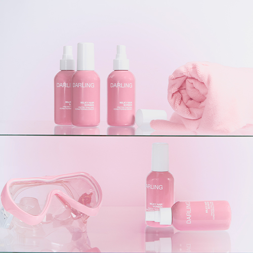 Meerdere roze flacons van Darling Milky Hair Screen op glazen planken, gestyled met een roze duikbril en een opgerolde roze handdoek.