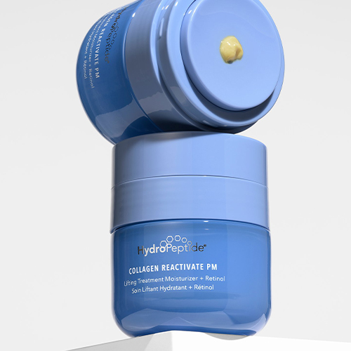 Twee blauwe potten HydroPeptide Collagen ReActivate PM nachtcrème op elkaar gestapeld tegen een witte achtergrond, waarbij op de bovenste dop een beetje gele crème te zien is.