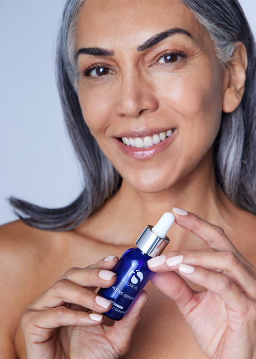 Een lachende vrouw die een flesje iS CLINICAL Active Serum in haar handen houdt.