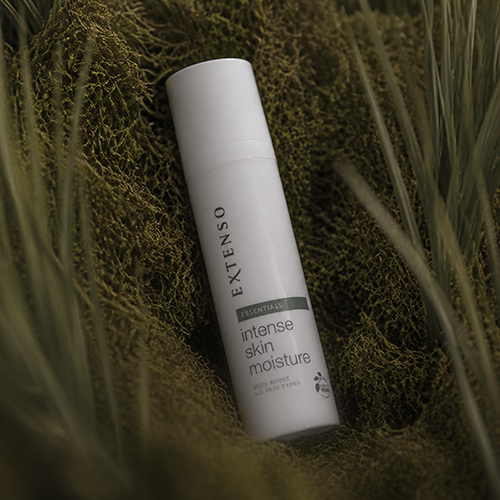 Sfeerfoto van de flacon Extenso Intense Skin Moisture (75ml) die in een groene, bemoste natuurlijke omgeving ligt.