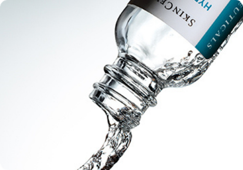 Een glazen fles van Skinceuticals waar vloeistof uit wordt gegoten voor hydratatie