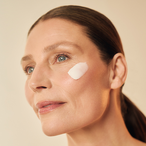 Een vrouw die een kleine dot witte Elastin gezichtscrème op haar jukbeen aanbrengt.