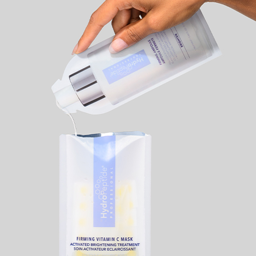 Handen die vloeistof uit een ampul gieten in de verpakking van het HydroPeptide Firming Vitamin C Mask.