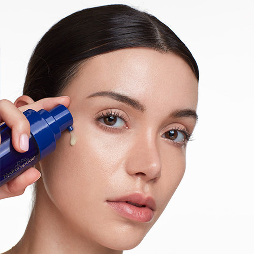 Een vrouw brengt het blauwe HydroPeptide Hydrostem serum aan op haar jukbeen met behulp van de pompflacon.