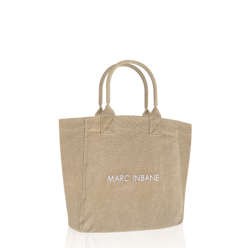 Een beige canvas tas van het merk Marc Inbane met witte geborduurde letters op een witte achtergrond met een lichte spiegeling aan de onderkant.