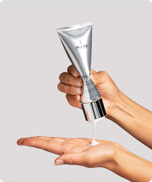 Een model knijpt een witte, romige cleanser uit de zilveren tube van IMAGE Skincare the MAX facial cleanser in een handpalm.