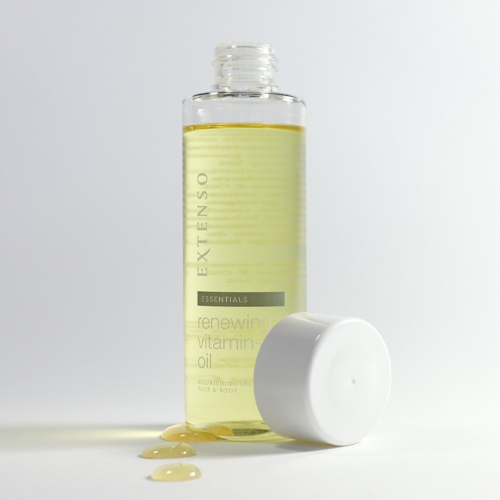 Een fles Extenso Renewing Vitamin E Oil zonder dop, met een paar druppels olie op de witte ondergrond ernaast.