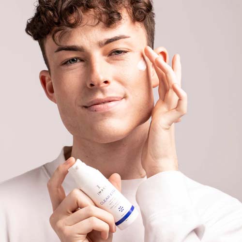 Een man brengt de Image Skincare Clear Cell Clarifying Repair Crème aan op zijn gezicht terwijl hij de flacon vasthoudt