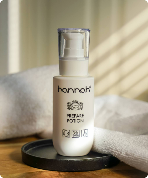 Een wit pompflacon van hannah Prepare Potion op een grijze stoffen ondergrond.
