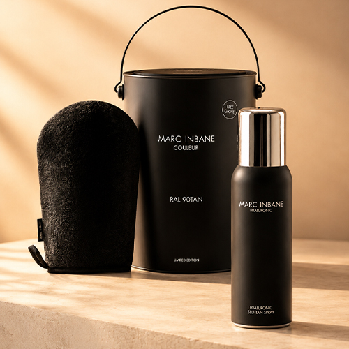 Sfeerbeeld van de Marc Inbane RAL 90TAN geschenkset met de Hyaluronic Self Tan Spray fles zwarte emmer en tanning glove op een stenen ondergrond met warme zonnestralen