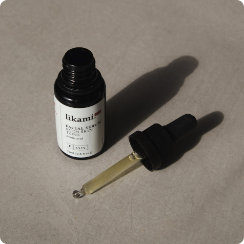 Een geopend donker glazen flesje van het Likami Even Skin Tone serum met de pipet ernaast op een grijze ondergrond. De afbeelding heeft afgeronde hoeken.