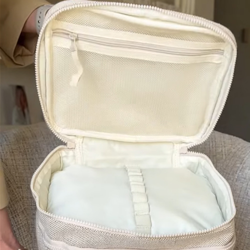 Een geopende, crèmekleurige beauty case van Extenso. De binnenzijde toont een ruim hoofdcompartiment met een elastische organizer-strip in het midden en een groot ritsvak van mesh in de deksel, ideaal voor het overzichtelijk opbergen van reisproducten.